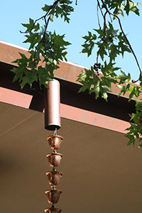 A brass chain of small cup hangs down from a roof's gutter