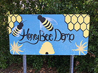 Handpainted sign that reads Honeybee Demo with blue background and bees