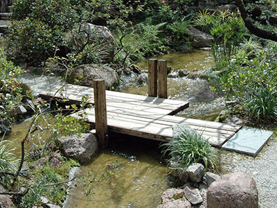 A flat wooden platform bridge crossing over a small stream