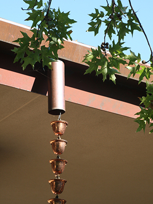 copper rain chain with bell-like attachments hanging from a gutter
