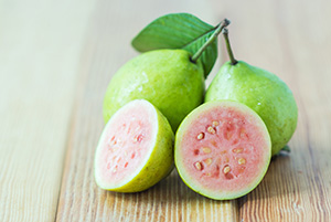Three small green guava fruits, one is cut in half to reveal pink flesh