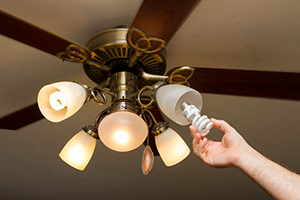 Hand putting new compact flurescent bulb in ceiling fan light fixture