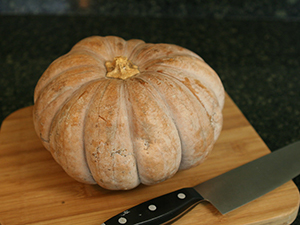 Orange-tan pumkin on cutting board with a large carving knife