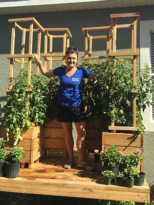 A woman standing on an attractive deck that includes planters for fruit trees and other potted plants