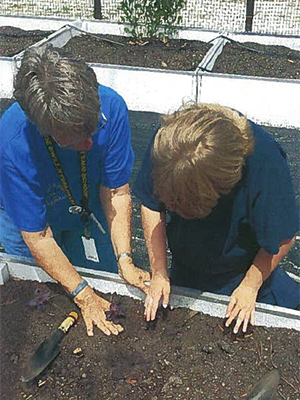 Student preparing soil for planting with assistance from a adult