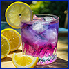 A glass containing a purple pink beverage along with ice and a lemon slice