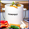 A small white container with the word compost on it, sitting on a cutting board with chopped vegetables