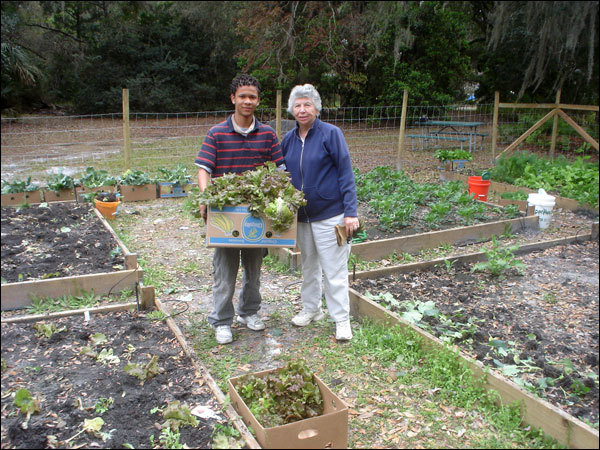 A young volunteer and a Master Gardener hold a box of produce in the garden.