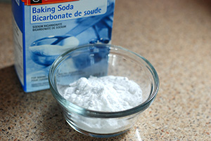 A small glass bowl of white powdery baking soda, the box nearby