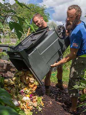 Two men dumping food waste into a compost pile