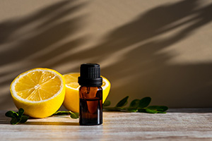 A small vial of essential citrus oil on a wooden table along with a yellow citrus fruit cut in half