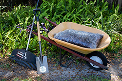 Wide rake, squared off shovel, and a wheelbarrow with bag of mulch in it
