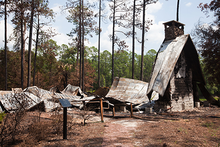The remains of a building destroyed by a forest fire, with nothing left but metal roofing and a stone fireplace