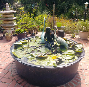A small raised up pond with lily pads and a small statue of a girl kneeling with egrets