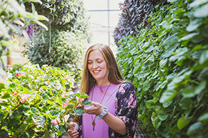 Smiling woman in greenhouse surrounded by walls of greenery with sunlight streaming down from above