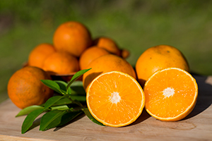 Pile of oranges on wooden table, one cut open to show flesh