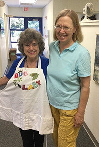 Betty in an apron reading Bug Lady in colorful letters and Celia standing next to her