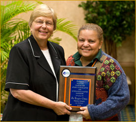 Two women smiling as the woman on the left presents the woman on the right with a plaque.