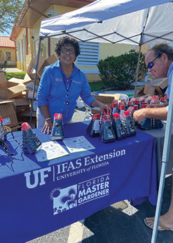 Smiling woman standing at a Master Gardener Volunteer table giving away mosquito traps
