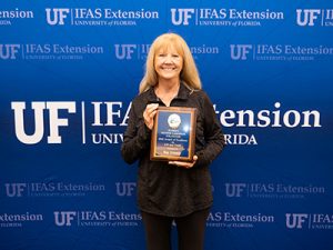 Representative from UF/IFAS Bay County smiling and holding the 4-H Youth award plaque.