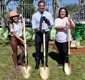 Two women and a man holding golden shovels outside in the sun