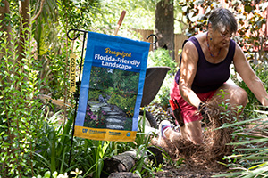 Woman working in her Florida-Friendly landscape with a gold-level flag displayed.