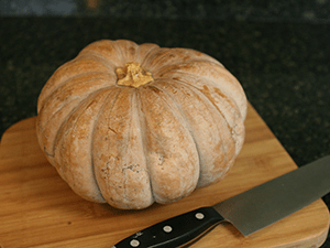 Orange-tan pumpkin on cutting board with a large carving knife