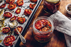 Dried tomatoes on a baking sheet, with some in a glass jar with oil. Photo by Vsevolod Belousov.