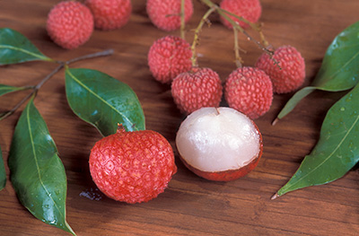 Lychee fruit on a cutting board, one peeled to reveal the translucent white flesh under the red bumpy skin.