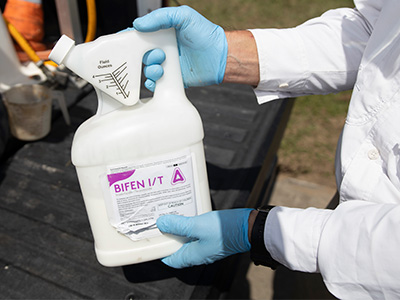 Gloved hands showing a container of pesticide about to be professionally mixed for use.
