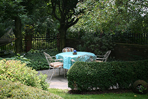 A patio with seating set off from the rest of the yard by a green shrub hedge.