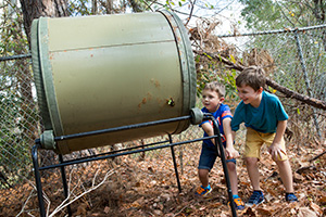 Two little boys turn a rotating compost bin
